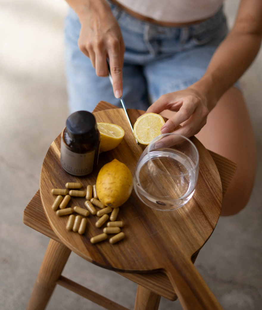 Mujer preparando suplemento natural con cápsulas y limón sobre mesa de madera, ejemplo de elección consciente y segura de suplementación femenina