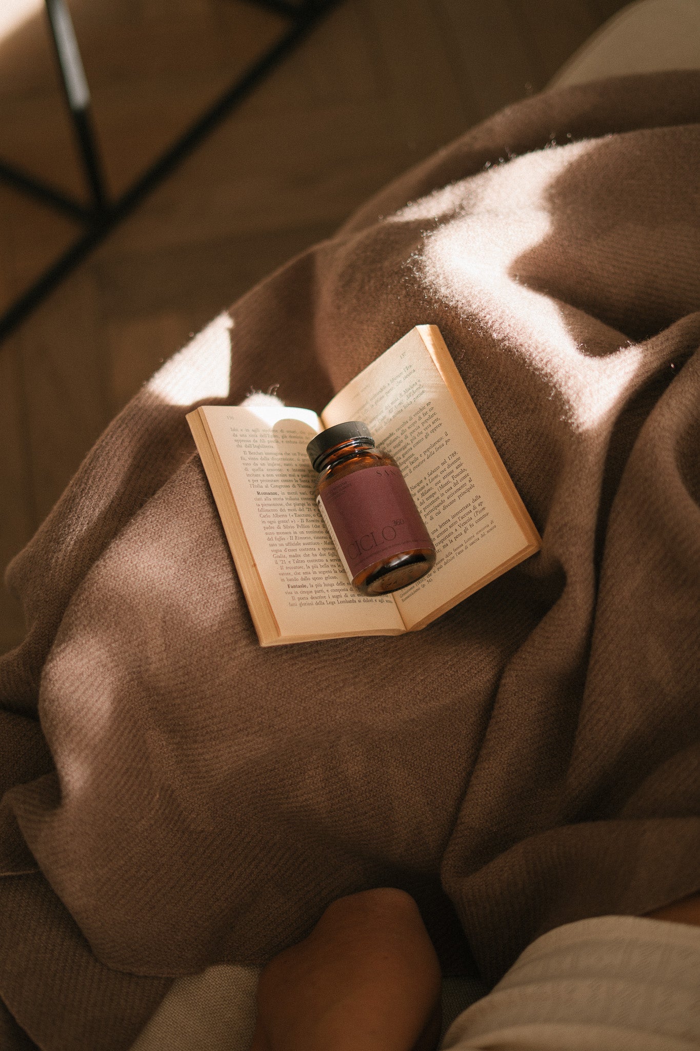 Ciclo 360 de SANA sobre libro y manta, suplemento natural para el ciclo menstrual y bienestar femenino