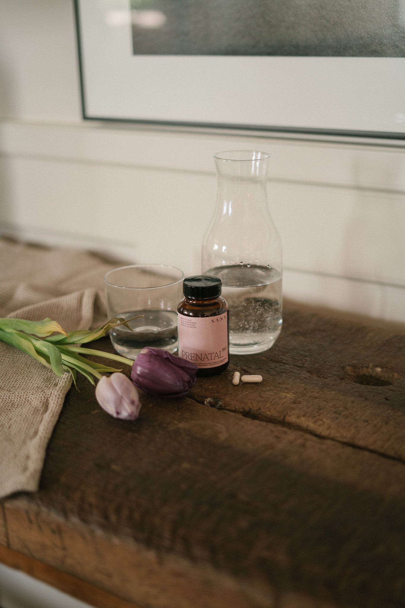 Suplemento prenatal Prenatal 360 de SANA Nutrients con cápsulas junto a vaso de agua en entorno natural para embarazo y fertilidad