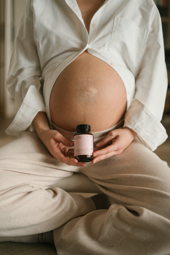 Mujer embarazada sosteniendo suplemento prenatal Prenatal 360 de SANA Nutrients sobre el abdomen durante el embarazo